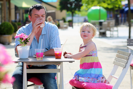 父亲和小女儿喝，吃在户外咖啡馆