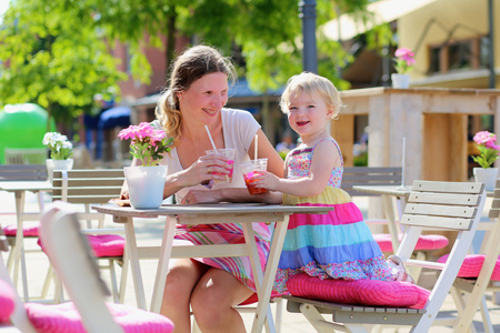 年轻的母亲和小女儿享受夏季饮料在户外咖啡馆
