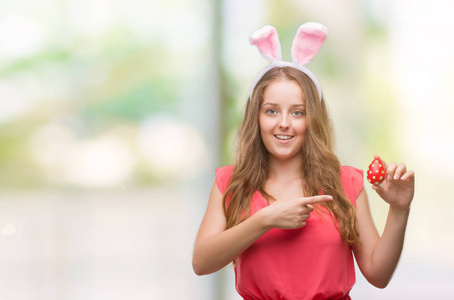年轻的金发女郎穿着复活节兔子耳朵很高兴指着手和手指