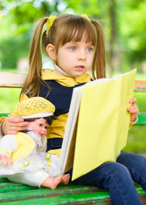 年轻漂亮的姑娘与她的娃娃读一本书