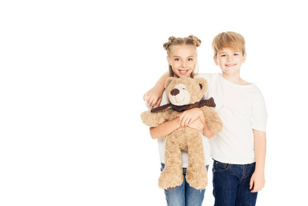 欢快的孩子拥抱, 抱着泰迪熊, 看着在白色的相机隔离