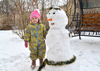 小女孩在院子里的雪人附近。