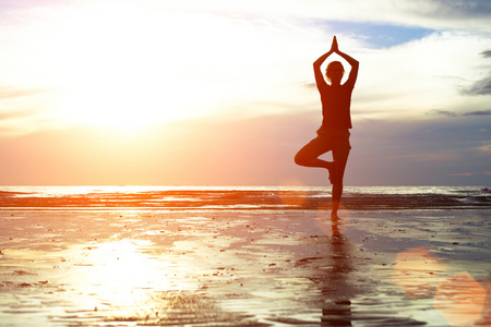 在日落时练瑜伽在海滩上的年轻女子