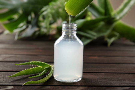 芦荟汁从叶子滴到木桌上的瓶子里照片