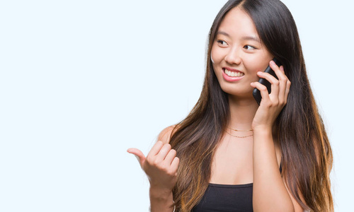 年轻的亚洲妇女在电话结束隔绝的背景指向和显示与拇指到边与愉快的面孔微笑