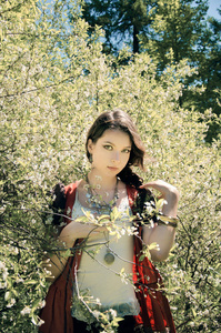 波希米亚风格的年轻妇女站在一个盛开的春天灌木的背景
