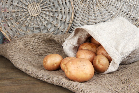 马铃薯在麻袋上麻布，柳条纸盒背景上的木桌上