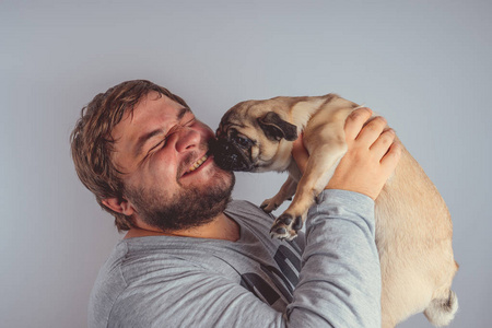一个带着胡子的男人在他怀里抱着一只可爱的小狗在灰色的墙上。人与狗之间的友谊概念