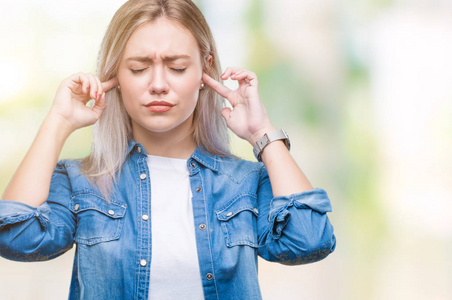 年轻的金发女人在孤立的背景覆盖耳朵与手指与愤怒的表达大声音乐的噪音。聋的概念