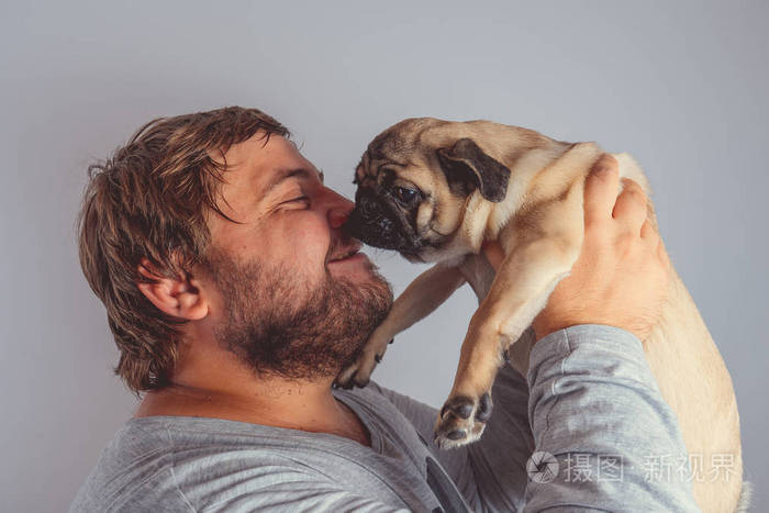 一个带着胡子的男人在他怀里抱着一只可爱的小狗在灰色的墙上.