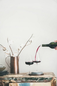 红酒从人的手里倒入酒杯在质朴的厨房台面上, 背后是白色背景