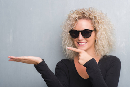 与卷曲的头发在垃圾灰色背景惊讶和微笑的相机时, 用手和手指指着照片