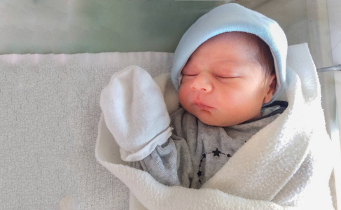 两天大的新生男婴, 睡在医院的婴儿床, 包覆在白色毯子