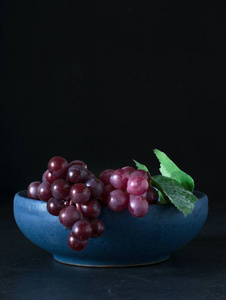 红色葡萄在一个蓝色的碗在黑暗的背景与复制空间为您的文本