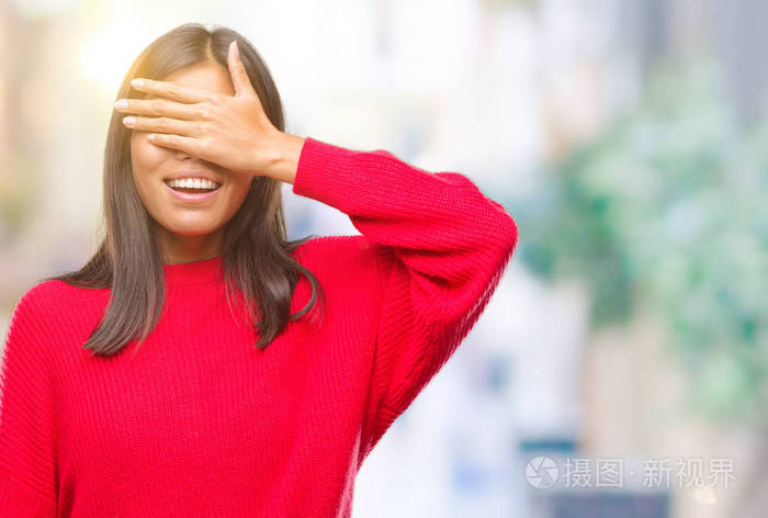年轻的亚洲妇女穿着冬季毛衣在孤立的背景下笑着笑着用手捂着眼睛惊讶