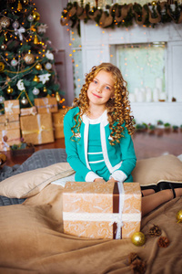 可爱的小女孩, 金色的卷发在家里附近的圣诞树与礼品和花环和装饰壁炉