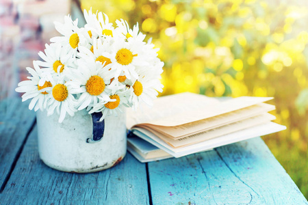 新鲜春黄菊的花束在乡村木桌户外与旧书的杯子