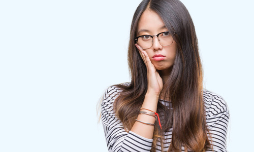 年轻的亚洲妇女戴着眼镜在孤立的背景下思维疲惫和厌倦与交叉手臂的抑郁症问题