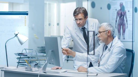 在个人计算机上高级医生和他的助手讨论病人的日志