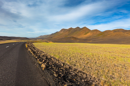 通过在蓝色夏季的天空下冰岛实地景观公路