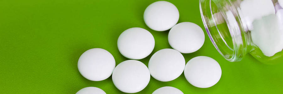 白色药片散落在绿色背景的玻璃瓶上照片