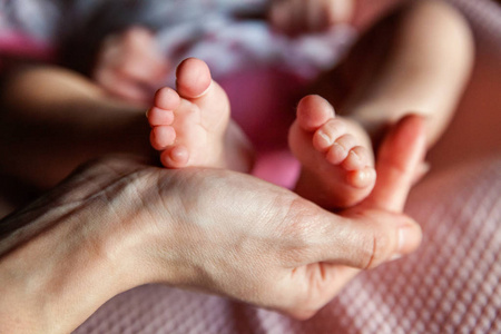 宝宝脚在母亲的手中。小初生婴儿的脚上女性异型手特写。妈妈和她的孩子。快乐家庭的概念。美丽的概念形象的产假
