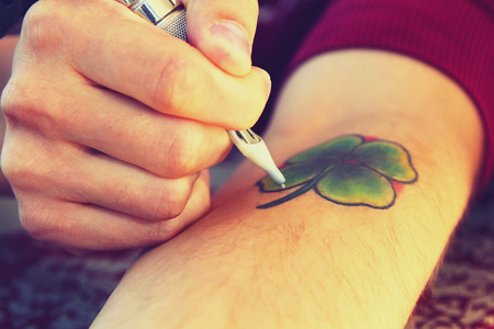 Tattooer 显示制作纹身的过程。纹身设计形式的四片叶子的三叶草