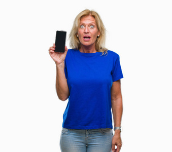 中年金发女子显示空白屏幕上的智能手机在孤立的背景惊吓与惊讶的脸, 害怕和兴奋与恐惧的表情