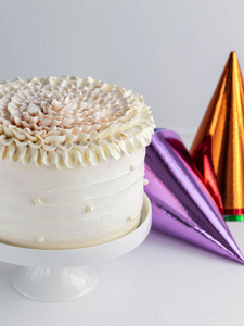 白色生日蛋糕与五颜六色的党帽在一个中立的背景。垂直。复制空间。庆祝理念