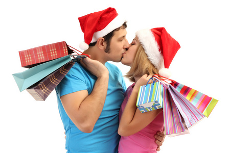 对年轻夫妇在圣诞老人的帽子购物和持有许多孤立在白色的购物袋