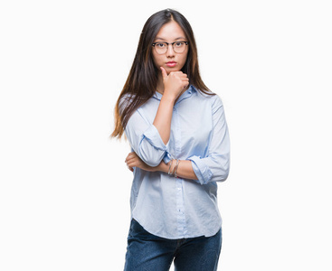年轻的亚洲商业妇女戴着眼镜在孤立的背景下, 看着自信的相机与交叉的手臂和手举起下巴。积极思考