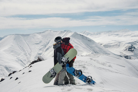 女孩和男孩站立和亲吻在山与滑雪板在令人惊奇的美丽的背景天空