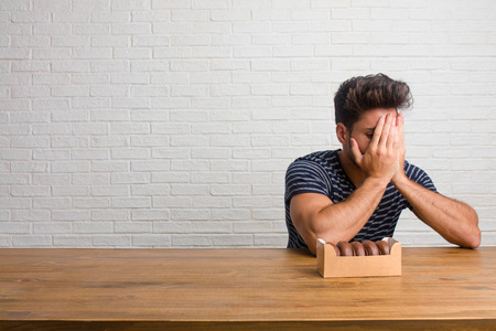 恐惧担心坐在桌子上的年轻帅哥感到担心和害怕, 看着和覆盖着脸, 恐惧