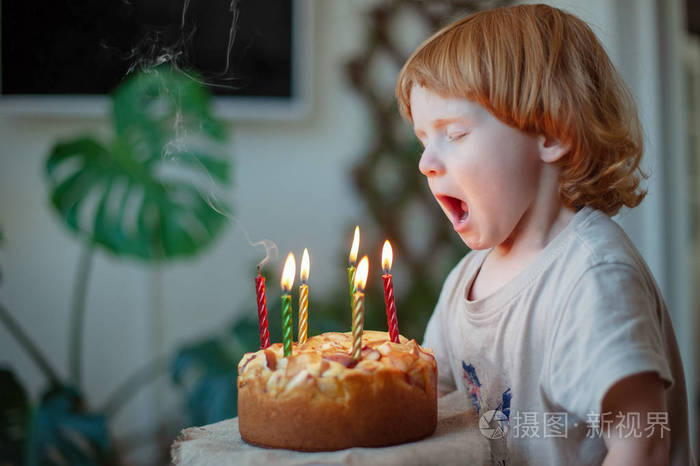 红头发的孩子在生日蛋糕上吹蜡烛