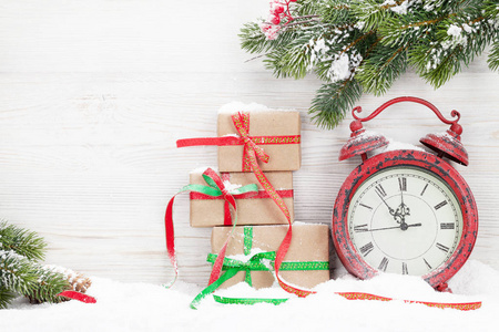 圣诞礼品盒, 闹钟和冷杉树枝覆盖在木墙前的积雪。使用复制空间查看