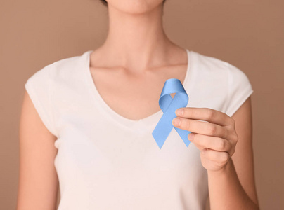 在颜色背景上持有蓝色丝带的妇女。前列腺癌意识概念