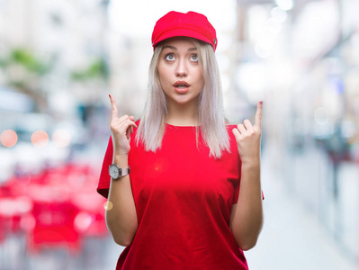 年轻的金发女子戴着红帽在孤立的背景惊讶和惊讶抬起手指和举起的胳膊