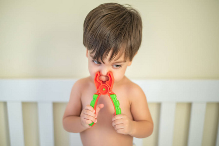 可爱的男婴幼儿在婴儿床玩具钳子在鼻子