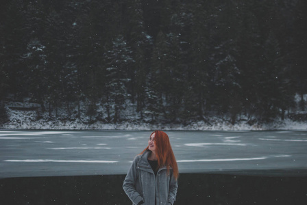 英俊的黑眼睛红头发的女孩站在山 Synevyr 湖和仰望的距离。雪花飘落在她美丽的秀发上。浪漫冬季概念
