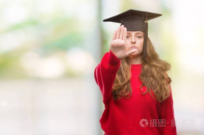身穿毕业帽的年轻金发女子用张开的手做停止标志以严肃和自信的表达, 防御手势
