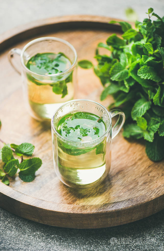 热草药薄荷茶饮料在木托盘上的玻璃杯与新鲜花园薄荷叶