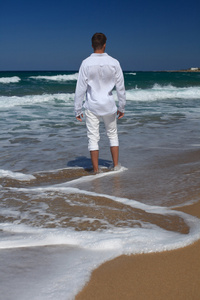 赤脚男子站在海滩上，从背面垂直观看