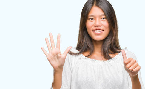 年轻的亚洲妇女在孤立的背景显示和指向手指数六, 而微笑着自信和快乐