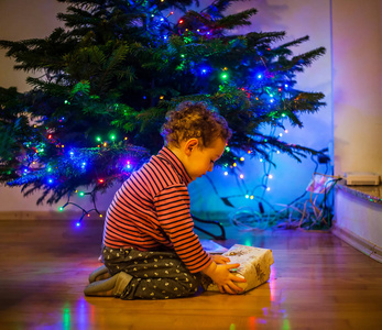 可爱的蹒跚学步的孩子在圣诞树附近的地板上打开礼物。