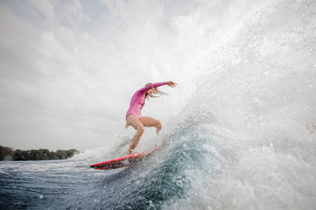 活跃的金发女子 wakesurfer 身着粉红色泳装骑下蓝色飞溅波对灰色天空在阴天