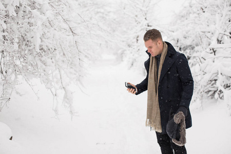 英俊的年轻人站在白雪覆盖的公园里, 拿着电话