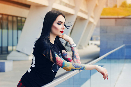 纹身的美。有吸引力的纹身的时髦女孩站在城市背景下的肖像