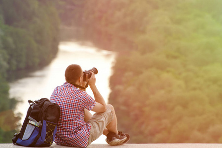 背包和山上的森林和河流背景拍照的男人。分