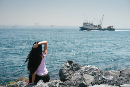 游客欣赏海景。积极的旅游。那个女孩看着船飘在天边
