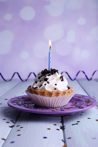 色木桌和浅色背景板上的蜡烛的生日杯蛋糕